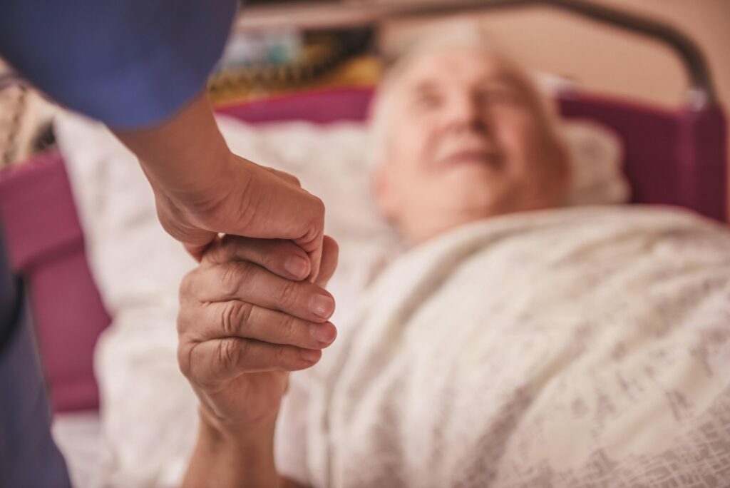 person holding elderly hand in hospital bed
